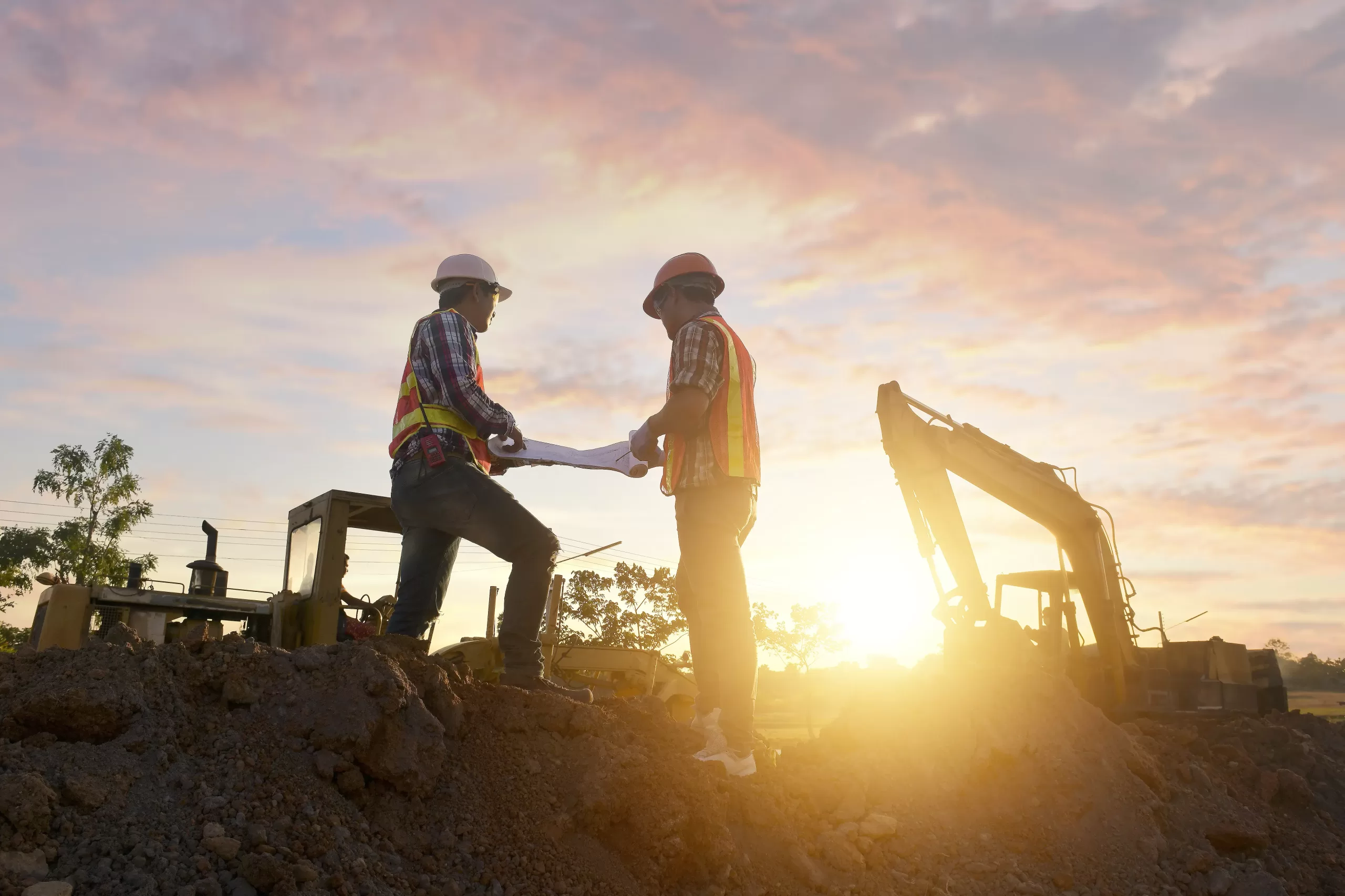 Engineers are working on road construction. engineer holding radio communication at road construction site with roller compactor working dust road on during sunset